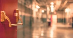 Corredor de escola com porta corta-fogo em primeiro plano e piso refletindo a luz