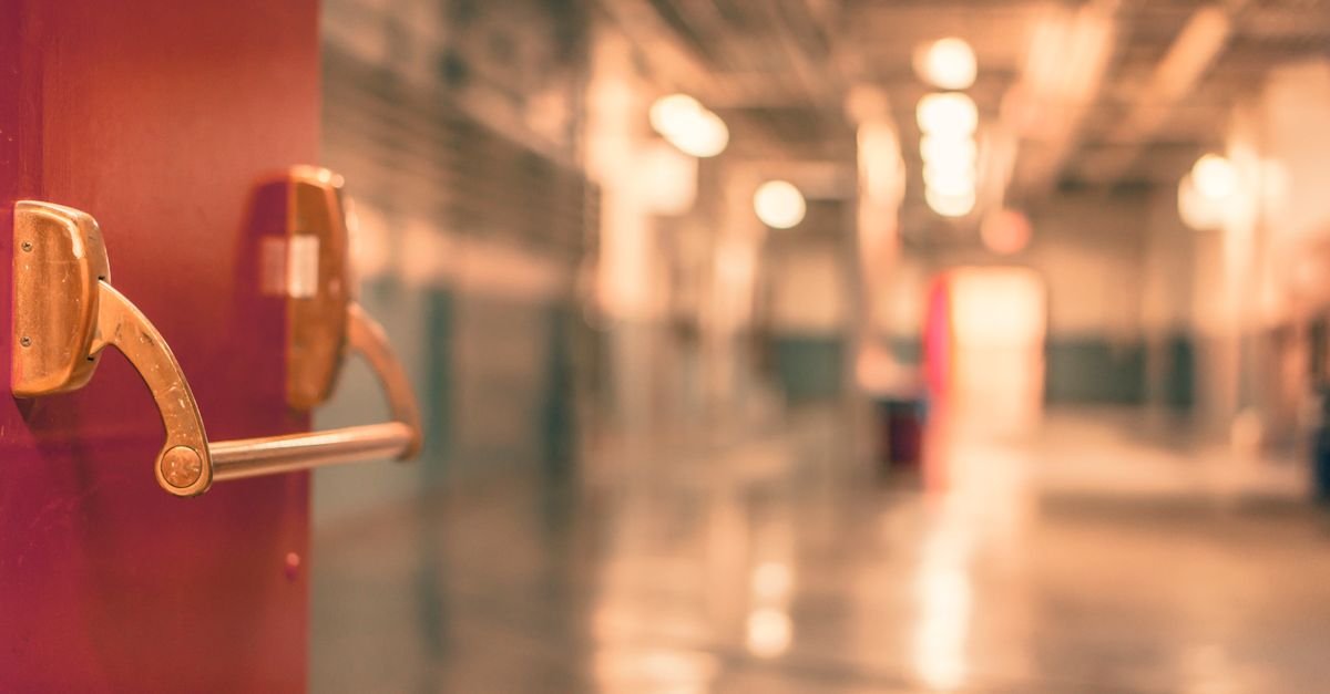 Corredor de escola com porta corta-fogo em primeiro plano e piso refletindo a luz