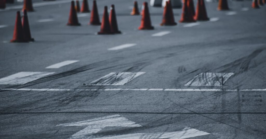 Cones laranjas de sinalização de trânsito espalhados sobre asfalto com marcas de frenagem e setas pintadas