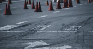 Cones laranjas de sinalização de trânsito espalhados sobre asfalto com marcas de frenagem e setas pintadas