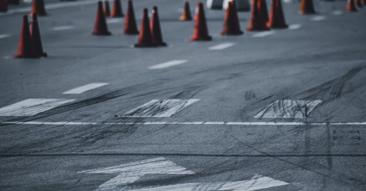 Cones laranjas de sinalização de trânsito espalhados sobre asfalto com marcas de frenagem e setas pintadas