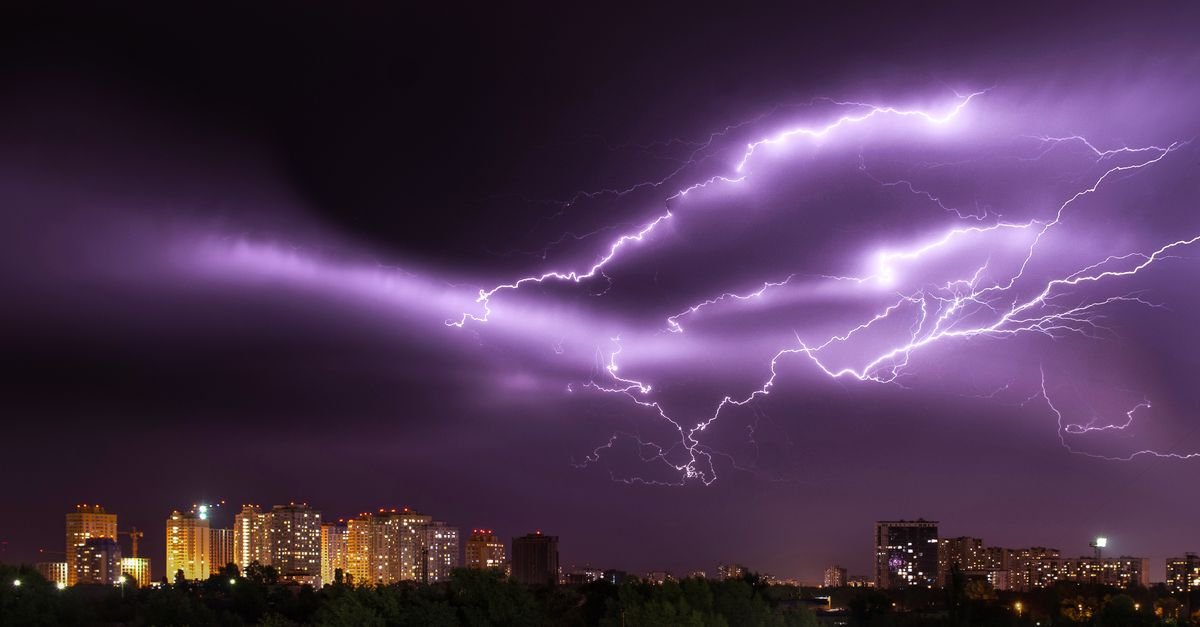 Raios cortam o céu à noite sobre uma área urbana com prédios iluminados