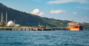 Navio petroleiro atracado em terminal aquaviário, com tanques e torres de refinaria ao fundo