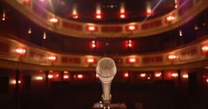 Microfone no centro de um palco de teatro com plateia e camarotes iluminados ao fundo