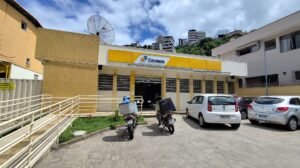 Fachada de agência dos Correios com letreiro amarelo e motos de entrega estacionadas