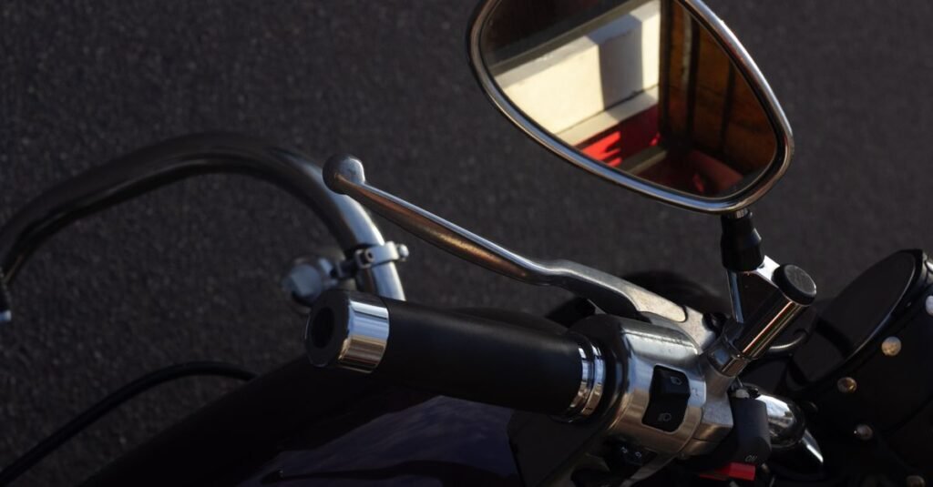 Guidão e retrovisor de motocicleta em close, com o asfalto ao fundo