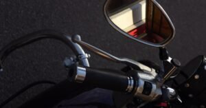 Guidão e retrovisor de motocicleta em close, com o asfalto ao fundo