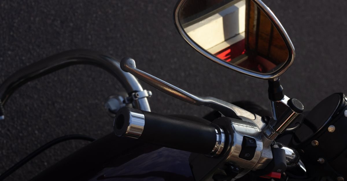 Guidão e retrovisor de motocicleta em close, com o asfalto ao fundo