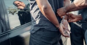 Homem sendo algemado por policial ao lado de veículo, em imagem ilustrativa de prisão em flagrante