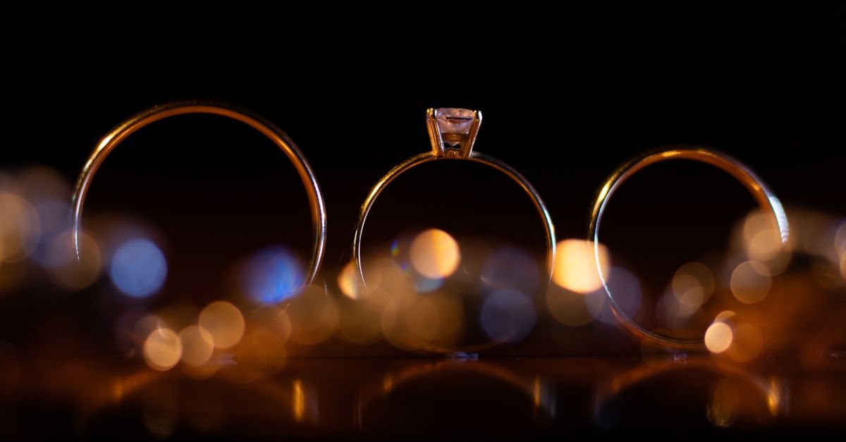 Três anéis de ouro em close, iluminados sobre fundo escuro
