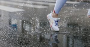 Pés de corredor com tênis esportivo pisando em poça de água no asfalto molhado