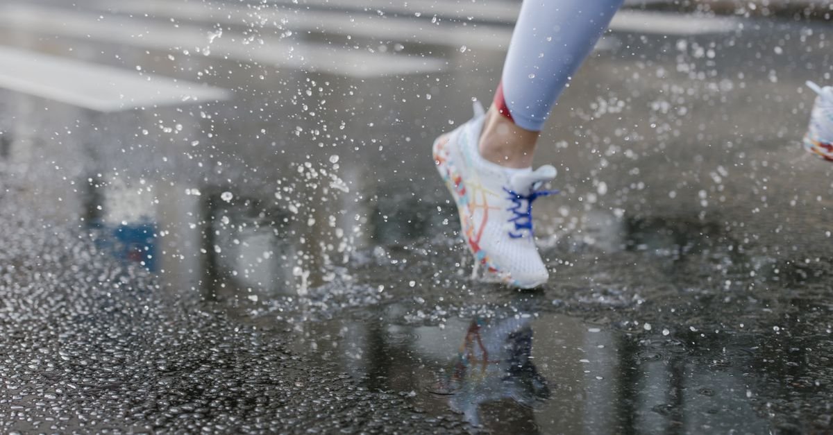 Pés de corredor com tênis esportivo pisando em poça de água no asfalto molhado
