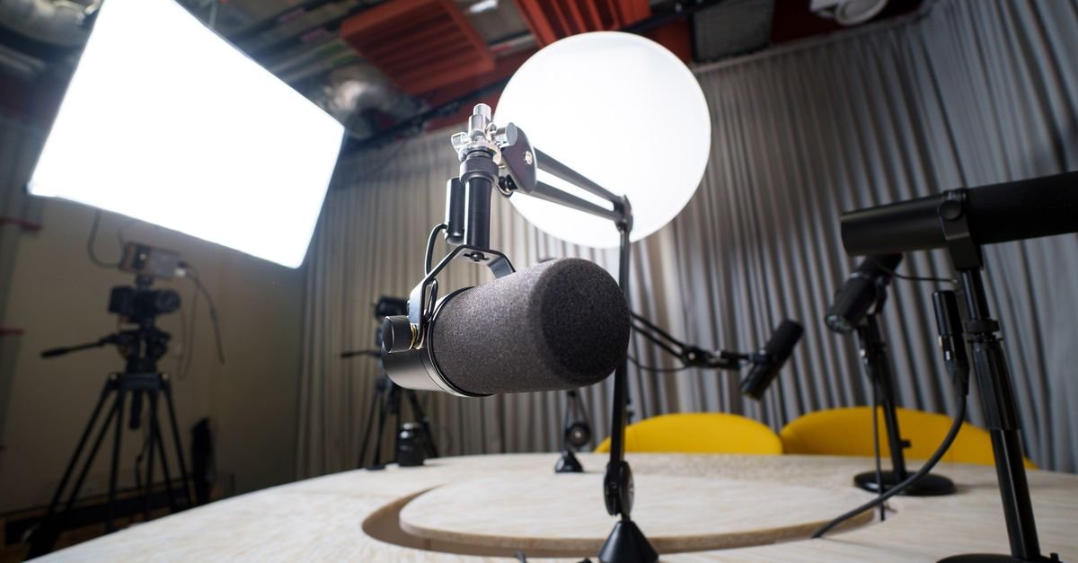 Estúdio de televisão com microfones sobre a mesa, câmeras e refletores acesos ao fundo