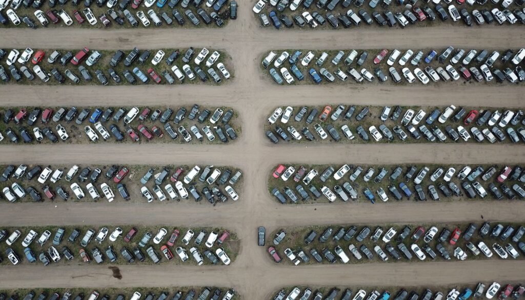 Vista aérea de pátio com centenas de veículos estacionados em fileiras separadas por corredores de terra