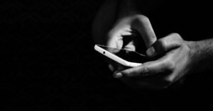 Mãos seguram um celular em fundo escuro, em imagem que ilustra o registro de ocorrencia por telefone