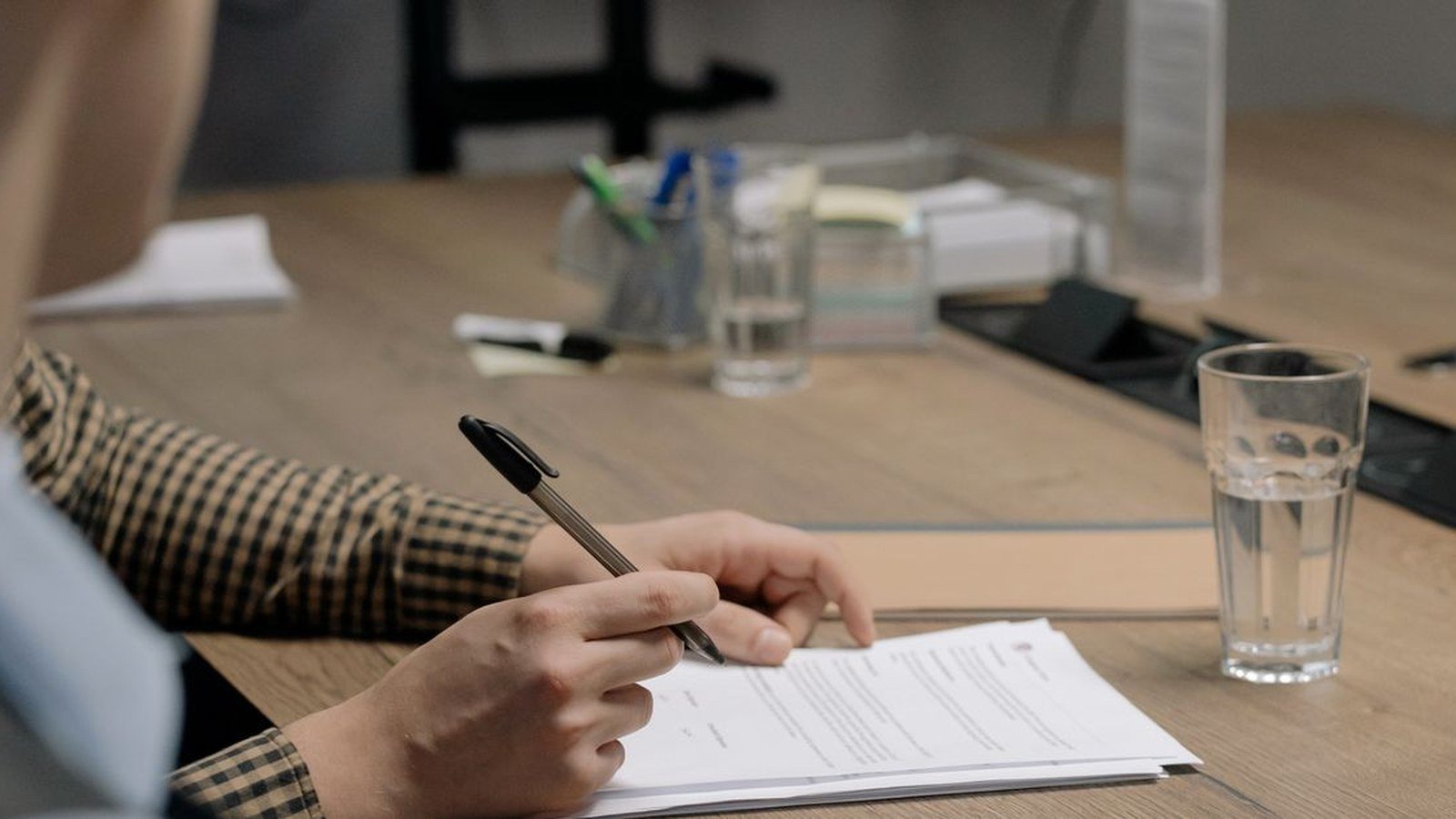 Pessoa assinando documento sobre mesa de escritorio com caneta