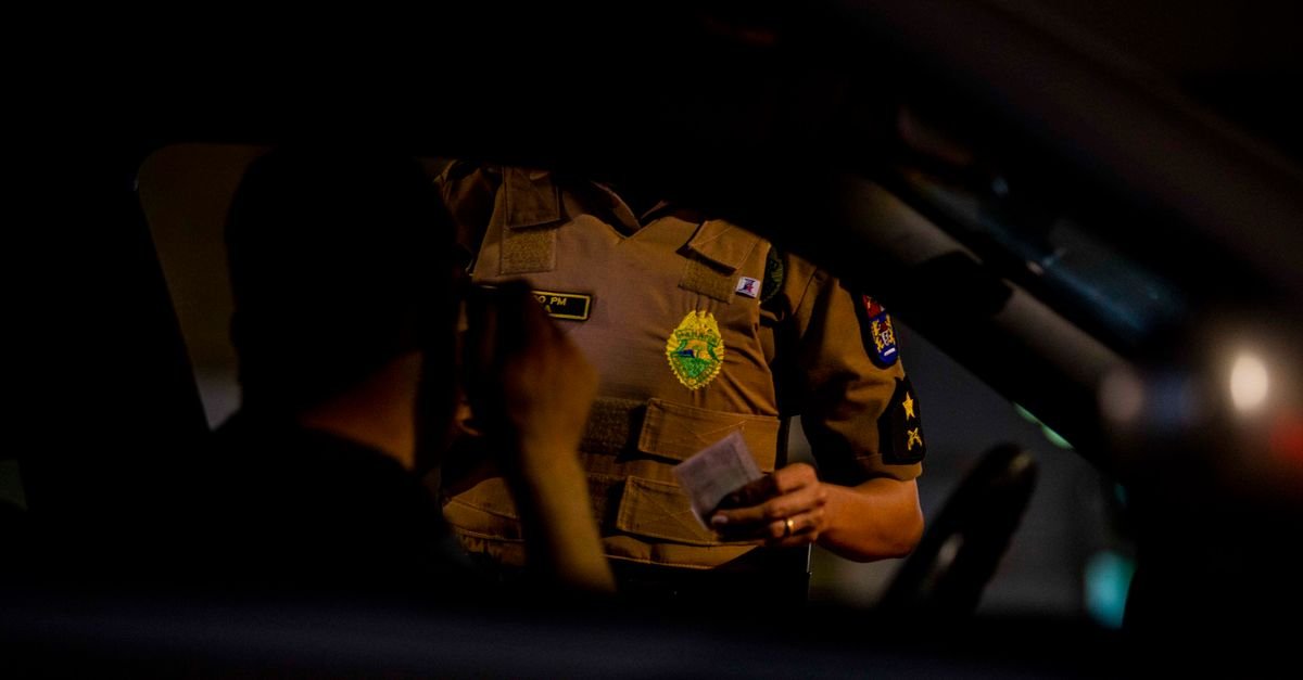Policial faz abordagem a motorista dentro do carro durante fiscalizacao de transito a noite