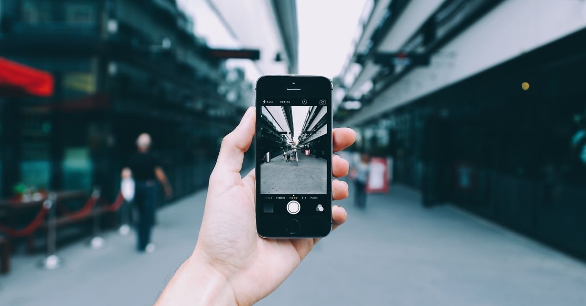 Mão segura celular fotografando uma rua urbana