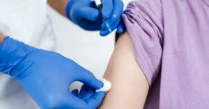 Profissional de saúde com luvas azuis aplica vacina no braço de uma pessoa
