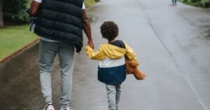 Pai caminha de mãos dadas com criança em rua arborizada