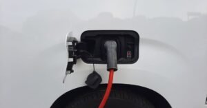 Cabo de recarga vermelho conectado à porta de carregamento de um carro elétrico branco