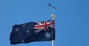 Bandeira da Austrália hasteada em mastro contra o céu azul, em imagem ilustrativa
