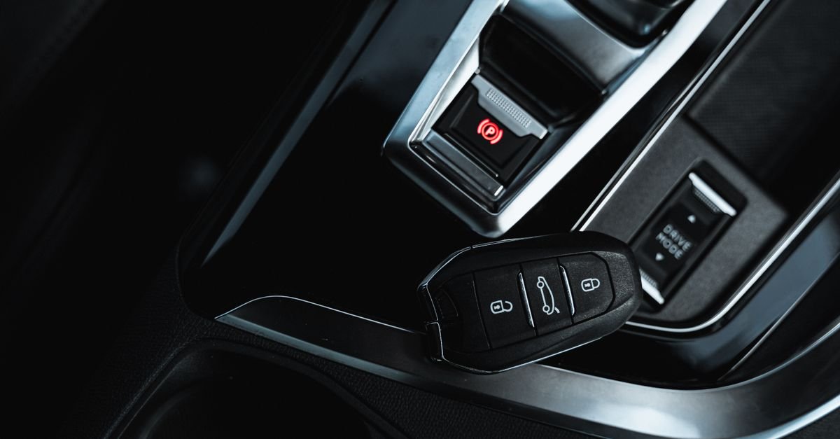 Chave de carro sobre o console central de um veículo, ao lado do botão de freio de estacionamento eletrônico