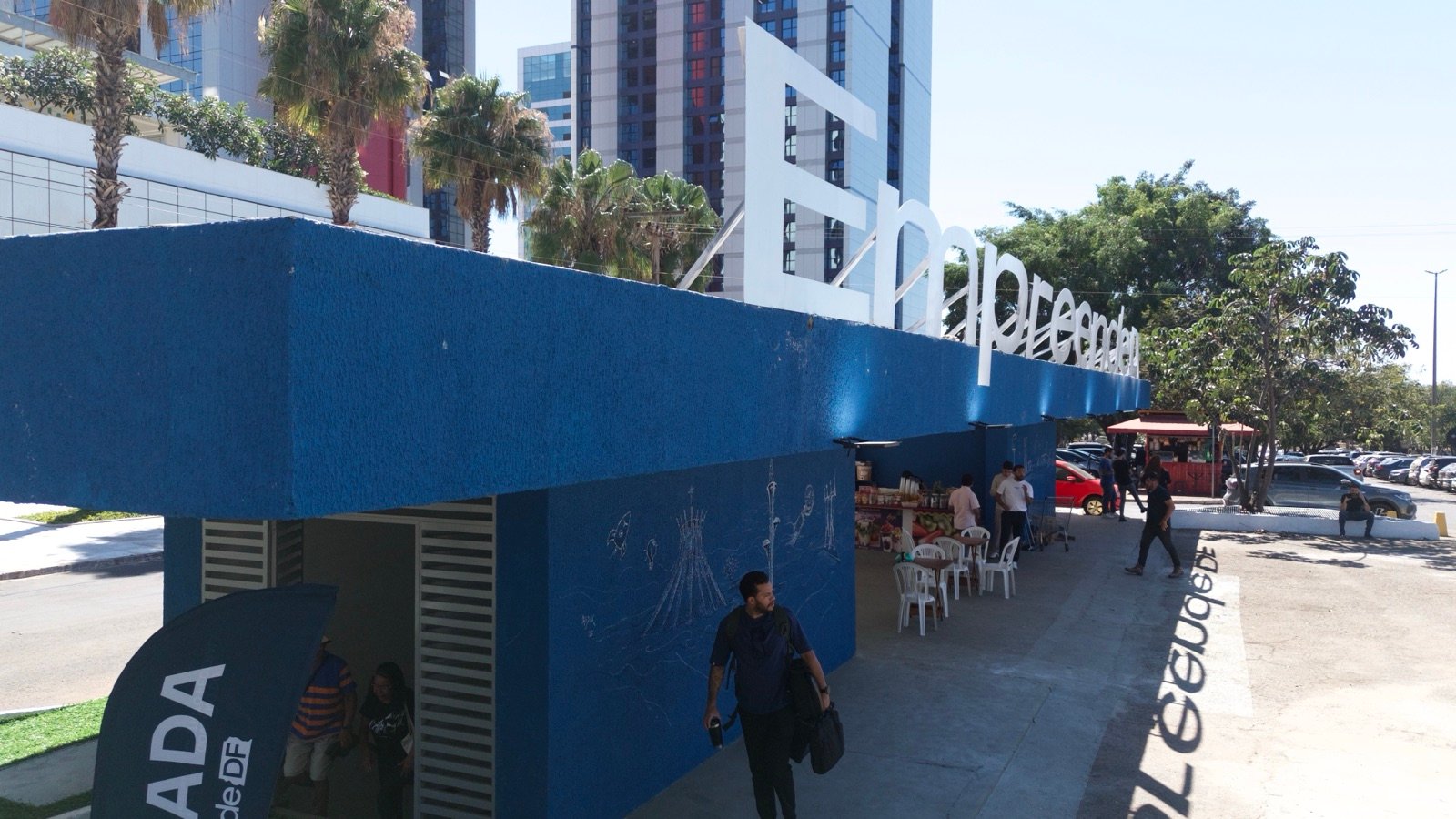 Fachada do hub EmpreendeDF em Brasília, com letreiro branco sobre estrutura azul e pessoas circulando
