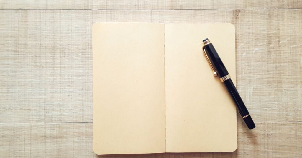 Caderno aberto em branco com caneta sobre mesa de madeira