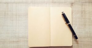 Caderno aberto em branco com caneta sobre mesa de madeira
