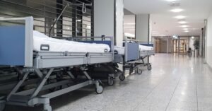 Corredor de hospital com macas vazias enfileiradas e iluminação acesa ao fundo