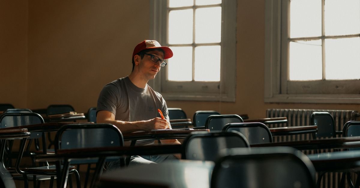 Estudante escreve em carteira de sala de aula vazia iluminada por luz natural