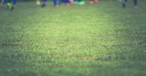 Gramado de campo de futebol com jogadores desfocados ao fundo