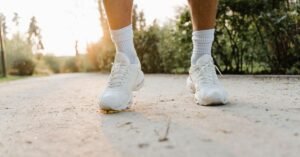 Close-up dos pes de uma pessoa caminhando de tenis branco por uma trilha de parque ao entardecer