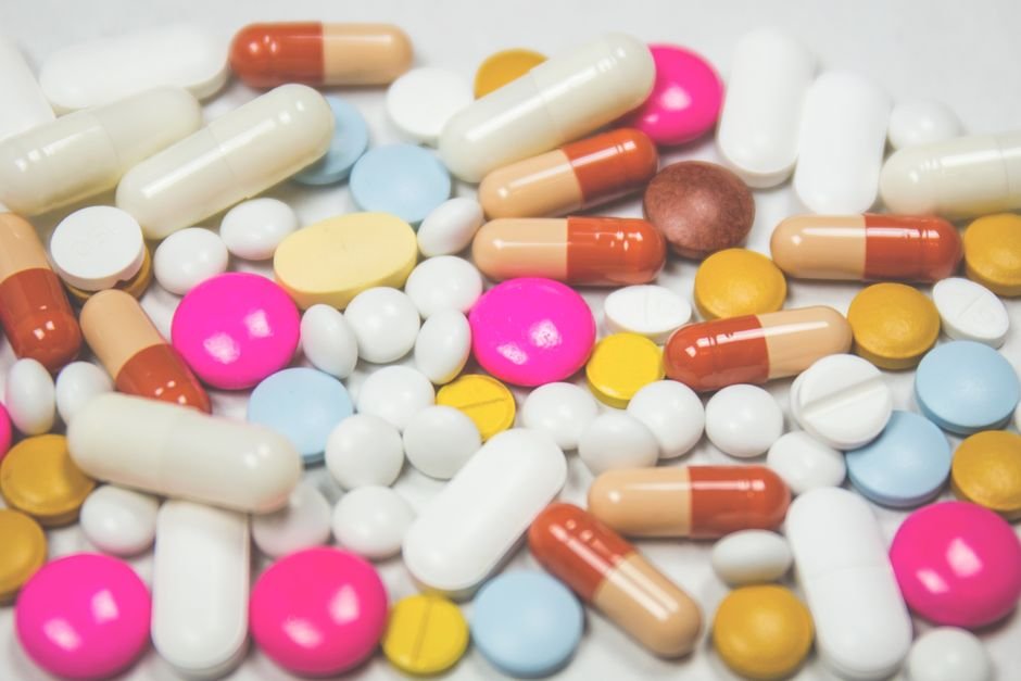 Comprimidos e cápsulas de diferentes cores espalhados sobre superfície branca