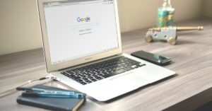 Notebook aberto sobre mesa de madeira com a página de busca do Google, ao lado de caderno e caneta