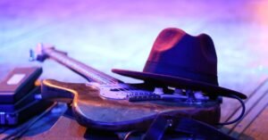 Guitarra elétrica e chapéu sobre o palco iluminado por luz roxa, ao lado de pedais