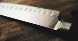 Faca de cozinha apoiada sobre superfície de madeira rústica, em close