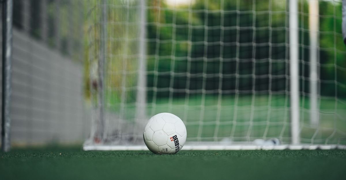 Bola de futebol parada na linha do gol em campo de grama