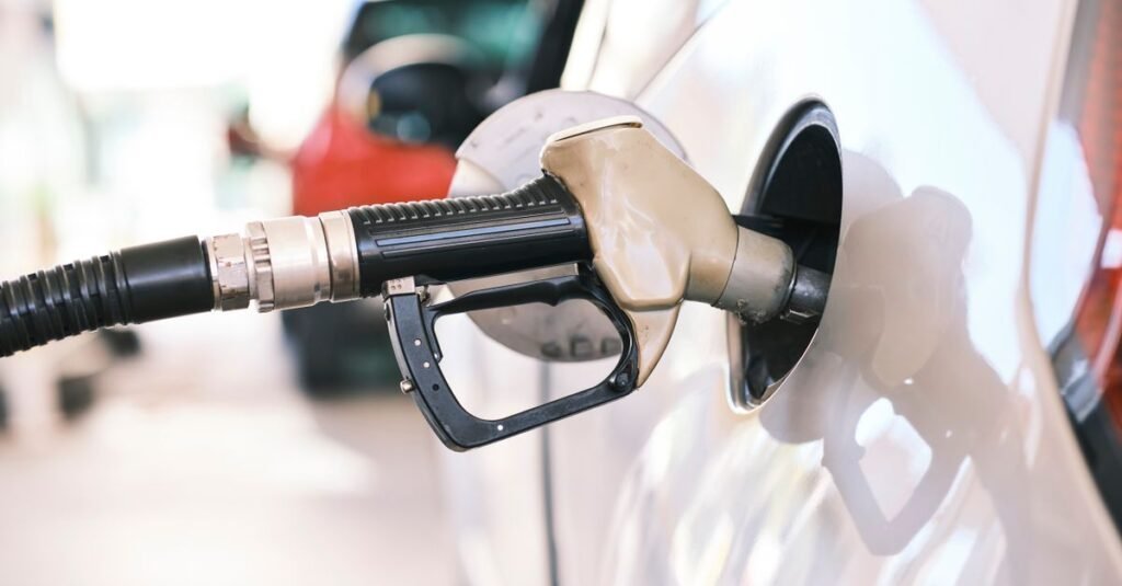 Bico de abastecimento preto inserido no bocal de tanque de um carro branco em posto de combustivel