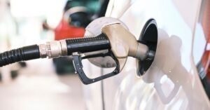Bico de abastecimento preto inserido no bocal de tanque de um carro branco em posto de combustivel