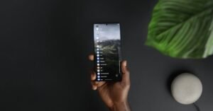 Mão segurando um smartphone com a lista de aplicativos na tela, sobre fundo escuro