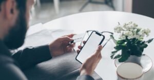 Homem segura cartão bancário em uma das mãos e celular na outra durante operação financeira