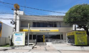 Fachada de agência bancária com placas de atendimento e entrada de vidro