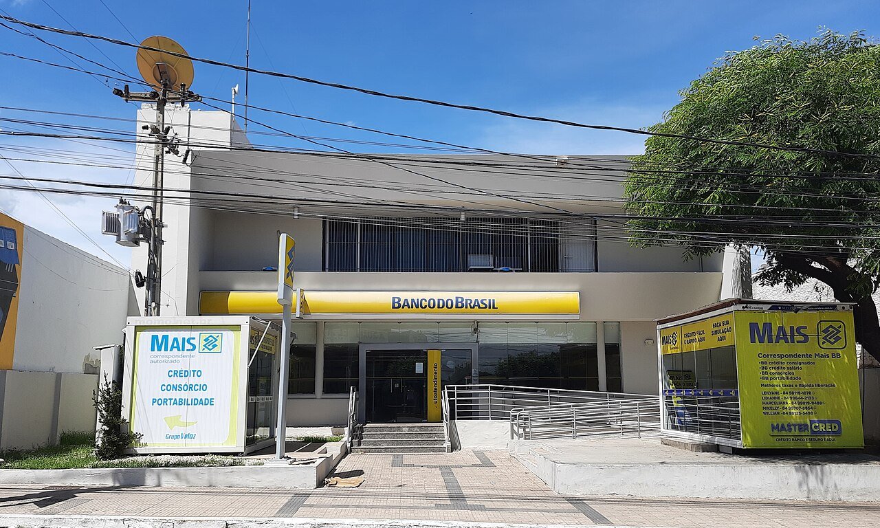 Fachada de agência bancária com placas de atendimento e entrada de vidro