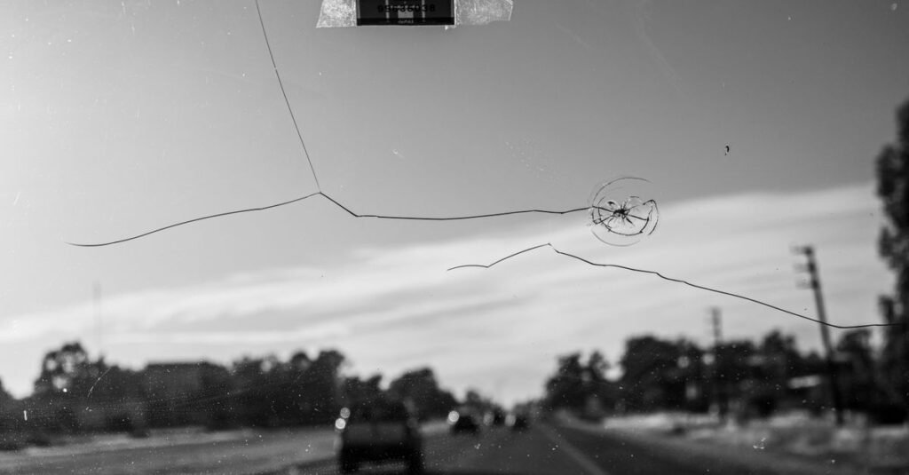 Para-brisa de carro trincado, visto do interior do veículo, em imagem em preto e branco
