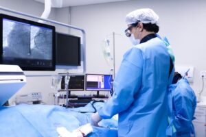 Equipe médica em sala de hemodinâmica do Hospital de Base do DF durante procedimento cardíaco, com angiografia coronária no monitor