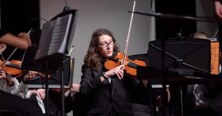 Violinista de terno preto tocando durante apresentação de orquestra em palco