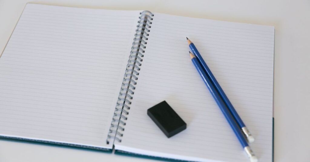 Caderno espiral aberto com dois lápis azuis e uma borracha sobre a mesa