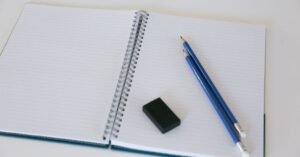 Caderno espiral aberto com dois lápis azuis e uma borracha sobre a mesa